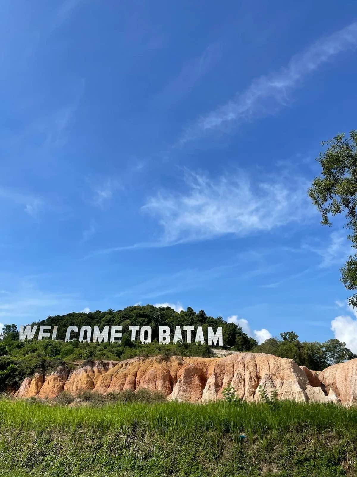 Giant white letters reading Welcome to Batam on a hillside above orange cliffs, Indonesia 2023