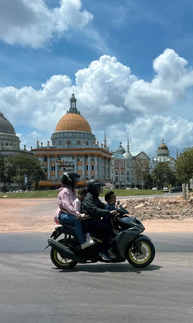 A family of four riding one scooter past a gold domed building, Indonesia 2023