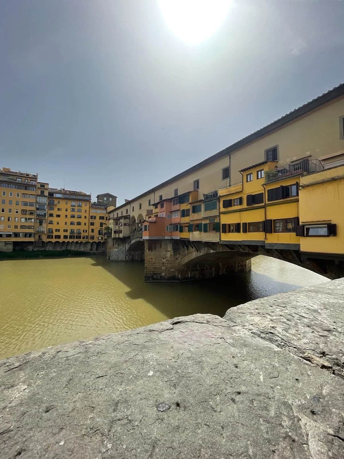 Shuttered yellow shops hanging off the Ponte Vecchio above the green river, Florence 2023
