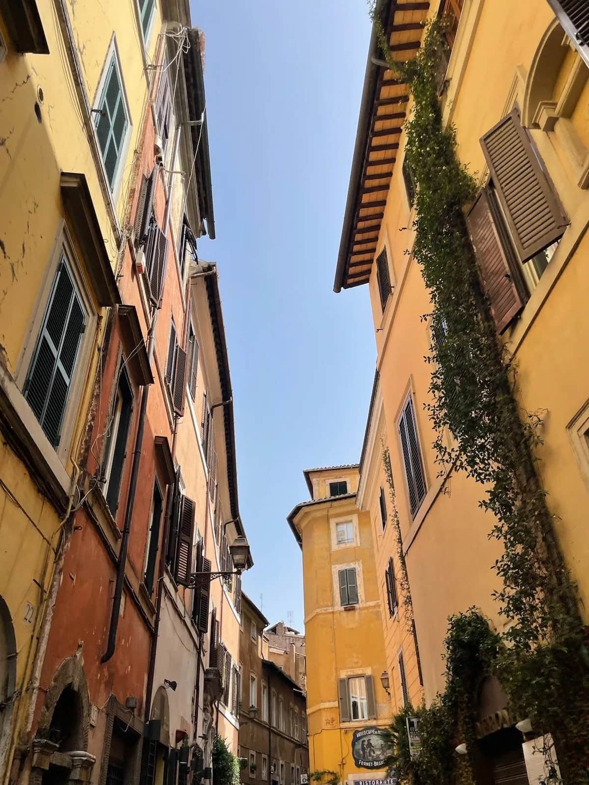 Yellow and red buildings with shutters leaning over a narrow lane, looking up, Rome 2023