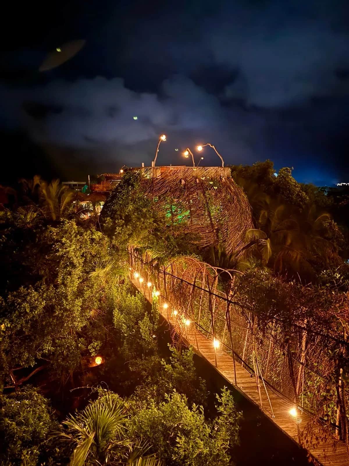 Lantern lit boardwalk winding through jungle to a thatched dome after dark, Azulik Tulum