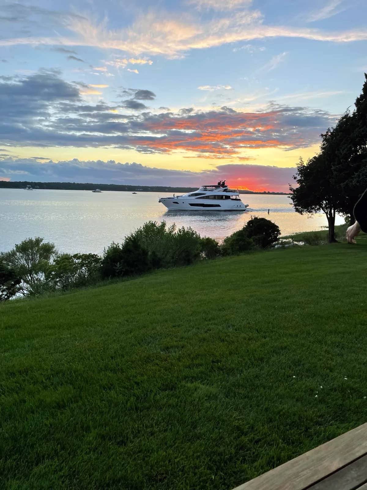 White motor yacht crossing the bay past a mowed lawn under burning orange cloud, East Hampton 2021