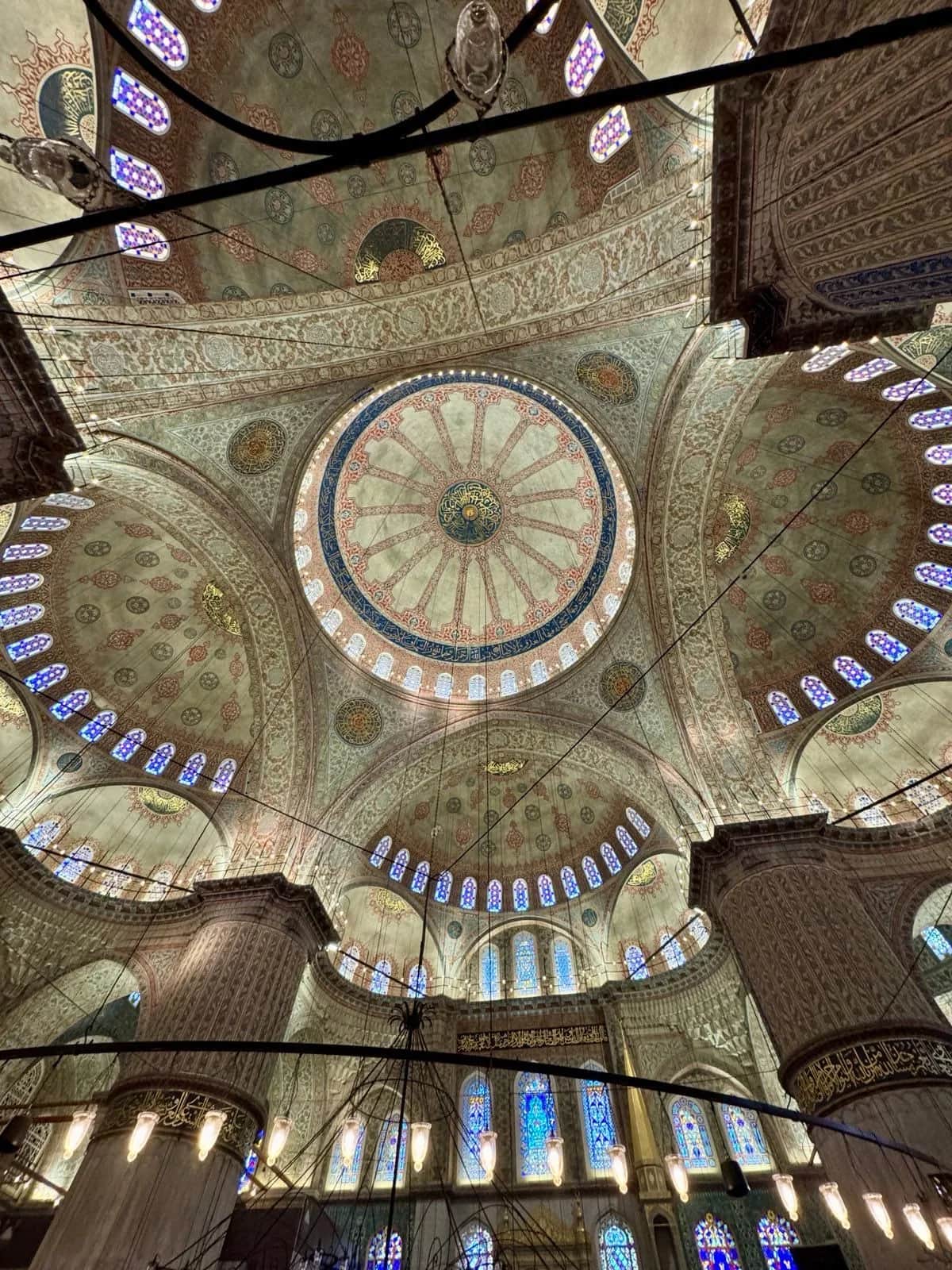 Painted domes and stained glass looking straight up inside the Blue Mosque, Istanbul 2024