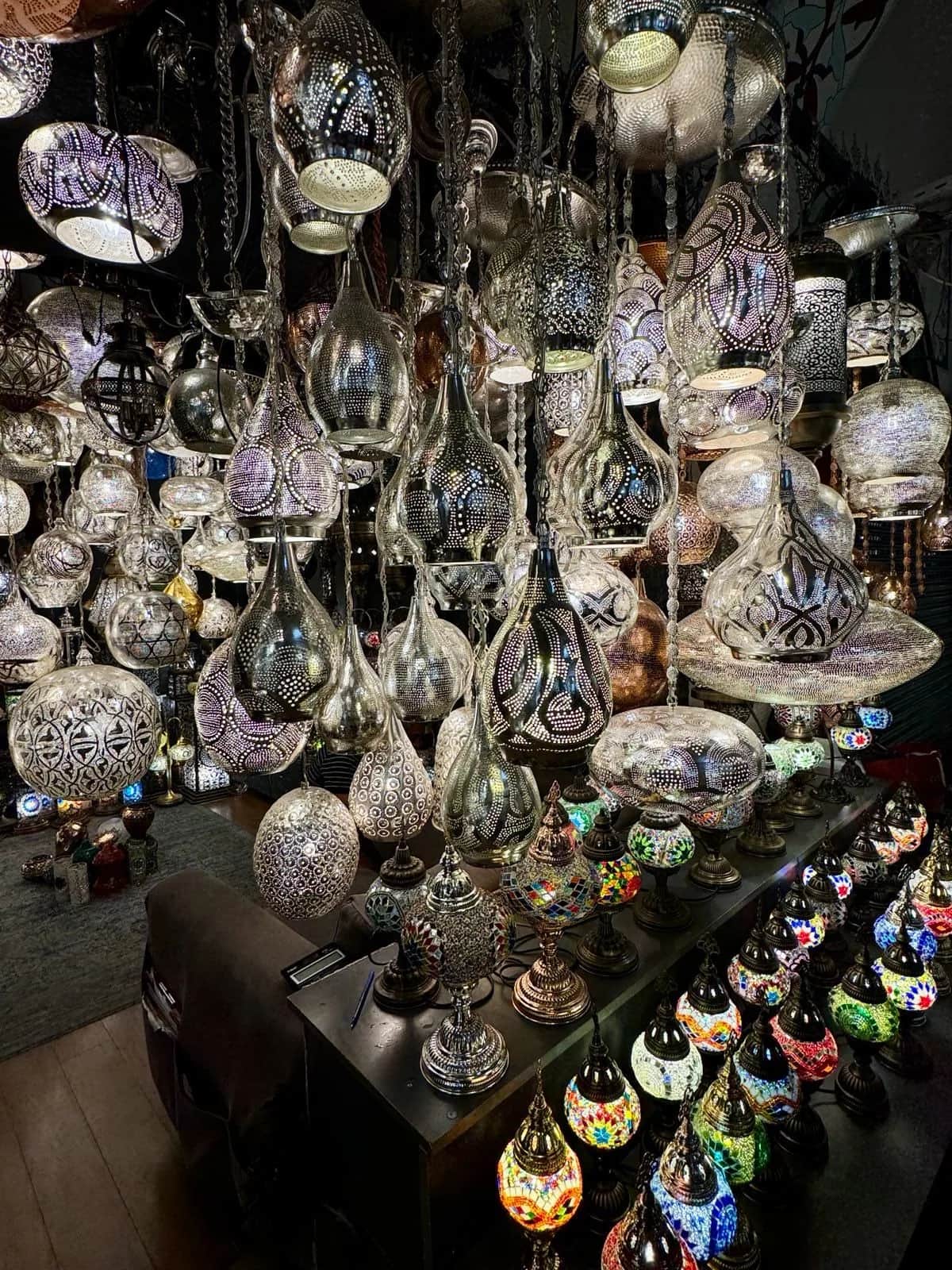 Silver pierced metal lanterns hanging above a table of small mosaic lamps in a shop, Istanbul 2024