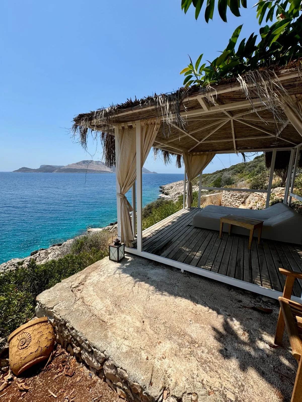 Thatched cabana with white curtains on a rocky cliff above the deep blue sea, Kas 2024
