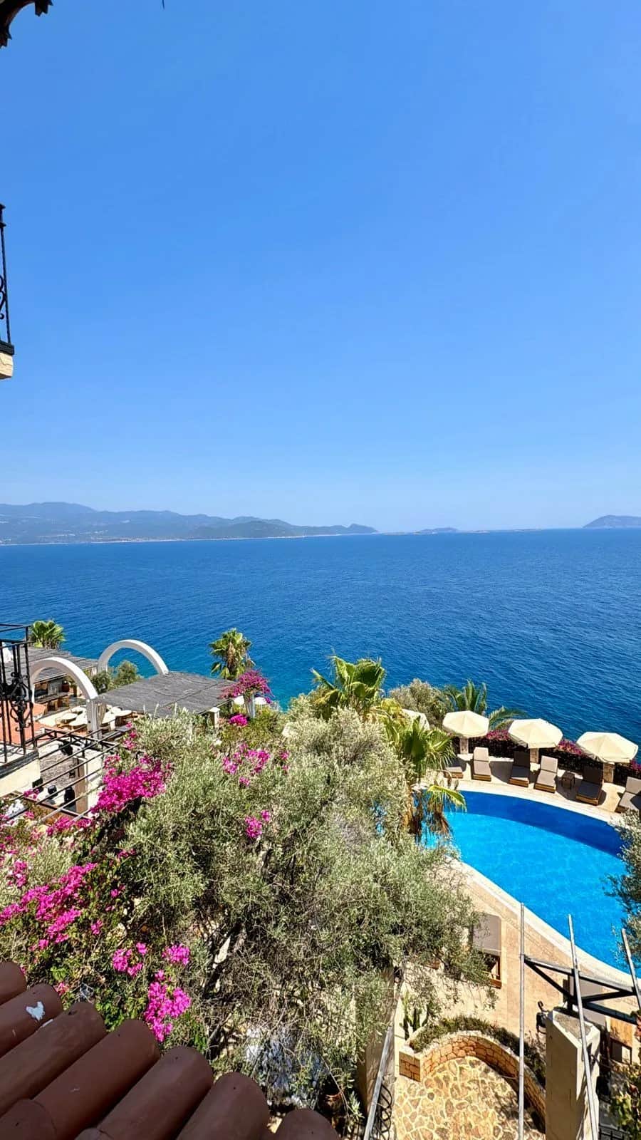 Hotel pool and white umbrellas below a terrace of pink flowers above the sea, Kas 2024