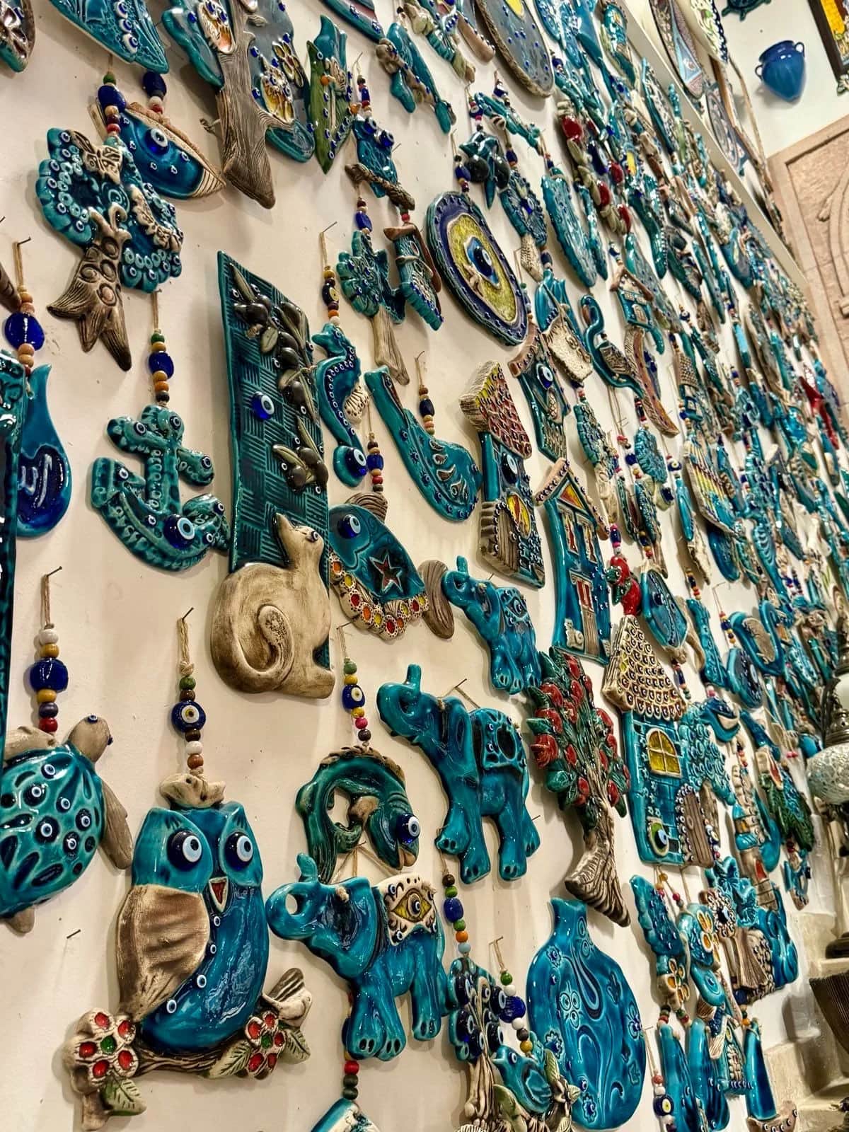Wall of turquoise ceramic charms, owls and elephants and blue eye beads, in a shop, Kas 2024