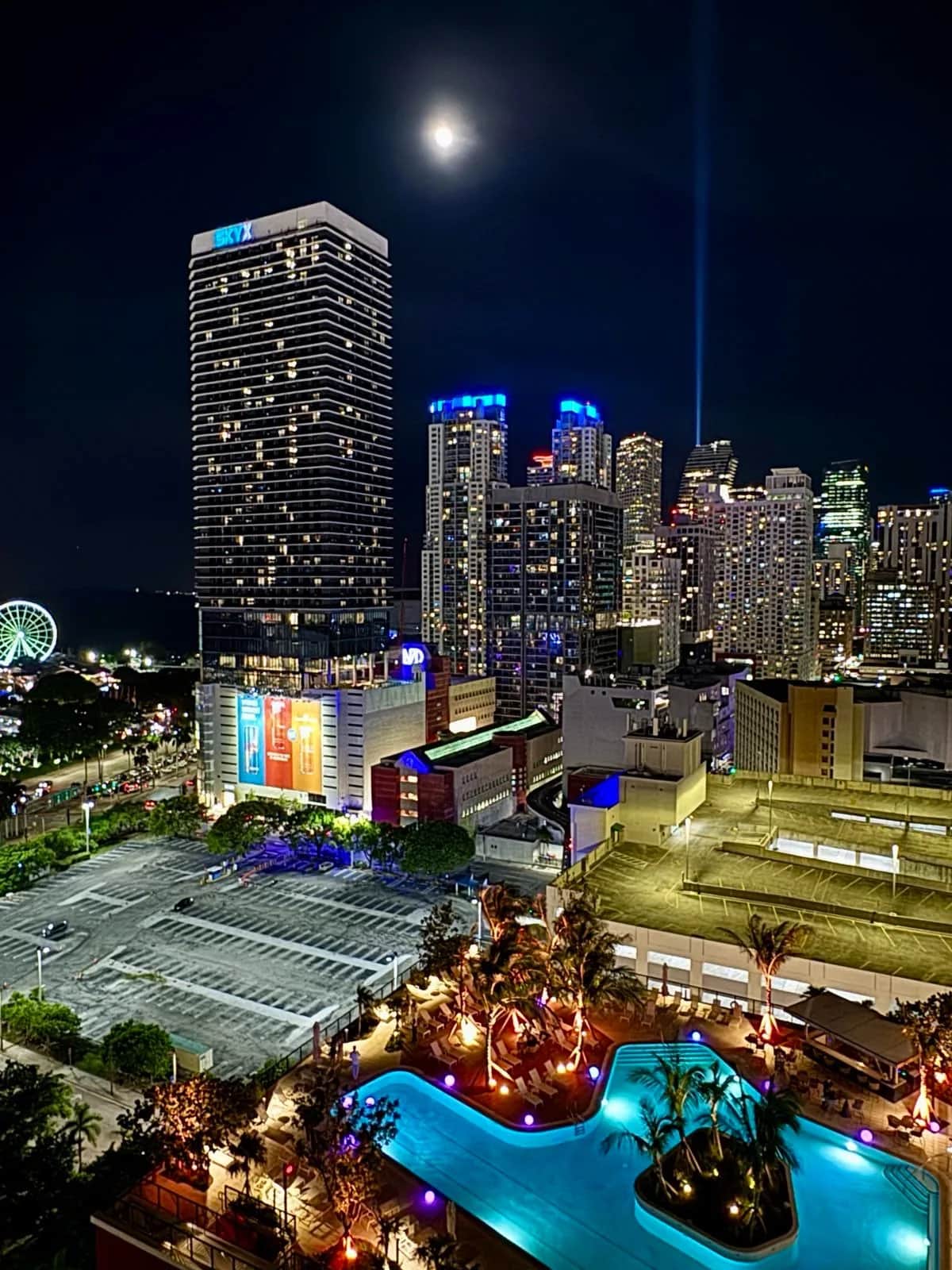 Downtown towers at night under a full moon with a lit hotel pool and palms below, Miami