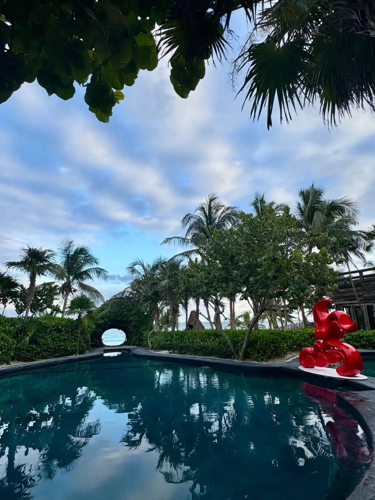 Pool at dusk with a red sculpture and a round hedge window onto the sea, Casa Malca Tulum