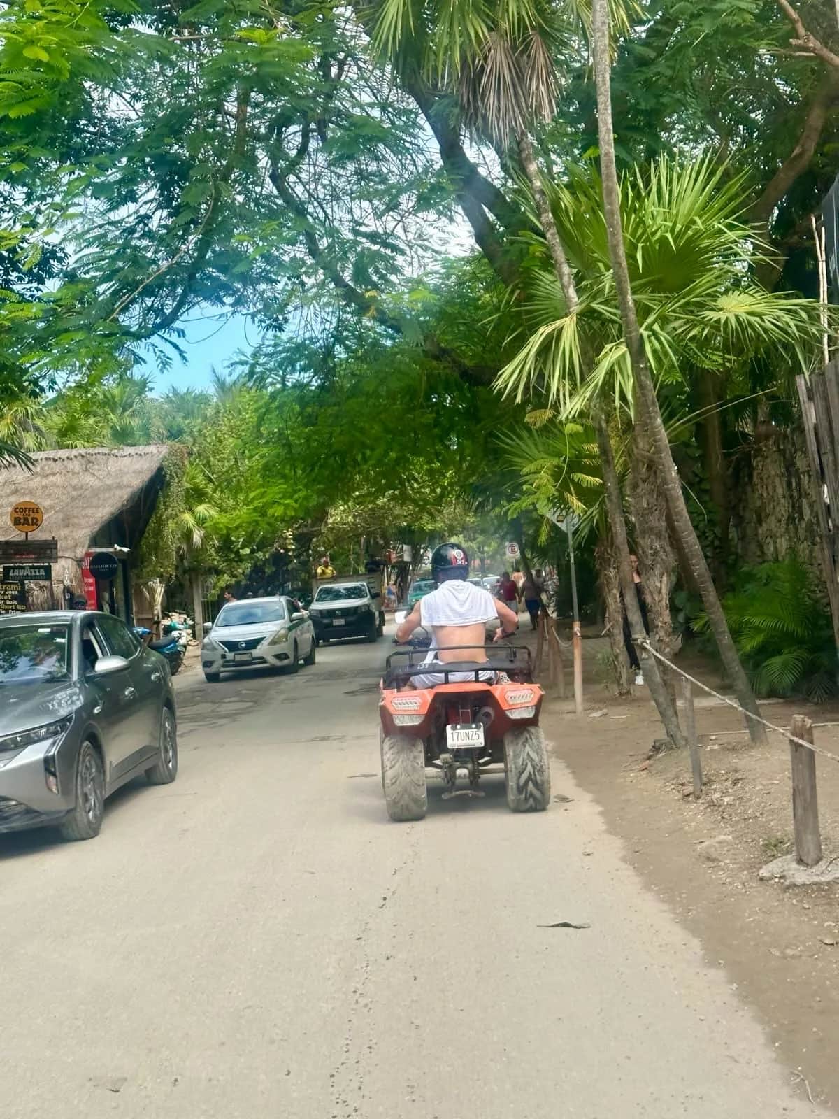 Rider on an orange ATV heading down the jungle road past a coffee bar, Tulum