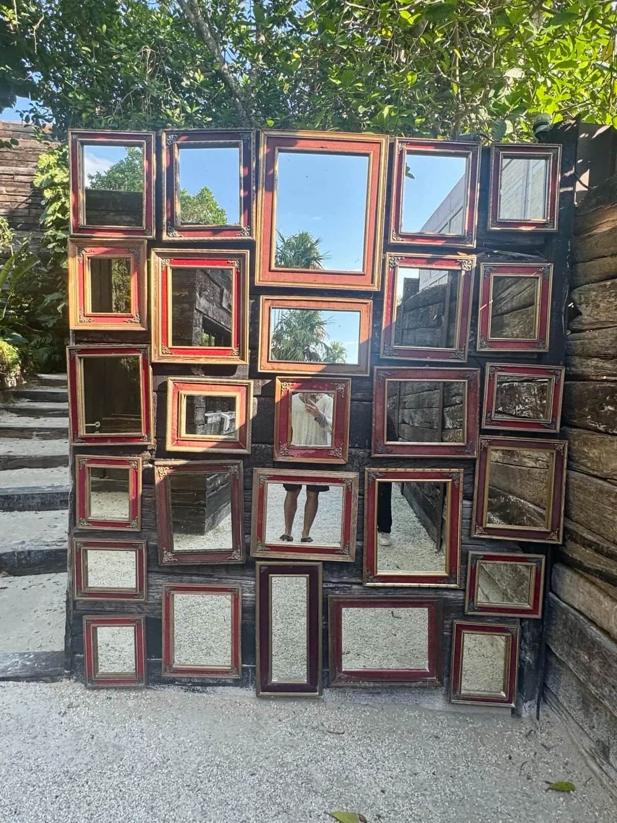 Wall of red and gilt framed mirrors on charred wood with the photographer reflected, Tulum