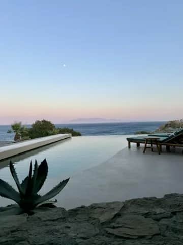 An infinity pool at dusk with an agave in the foreground and the moon over the sea, Greece