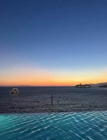 An infinity pool at sunset with a lit island on the horizon, Greece