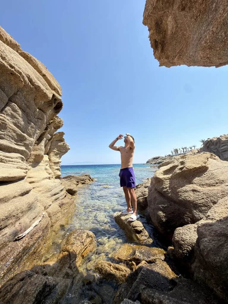 Standing on a rock in a sheltered cove of clear water beneath a sandstone overhang, Greece
