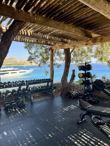 An open air gym under a timber pergola above a bay with a yacht at anchor, Greece