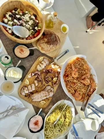 A long lunch of grilled fish, salad and greens laid out beside the water, Greece